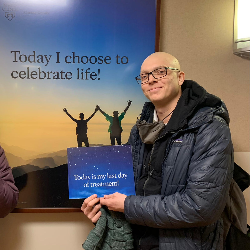 Person holding a sign with 'Today is my last day of treatment!' in front of a motivational poster.