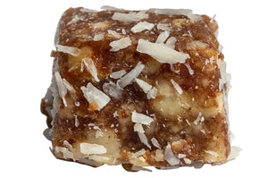 A single square energy bar or protein snack piece with a brown caramel-like center, chopped nuts, and shredded coconut flakes, photographed on a plain white background with a hard shadow.