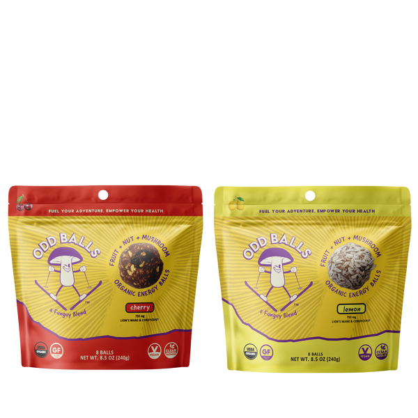 Two stand-up pouches of Odd Balls organic energy balls shown side by side on a white background. The left pouch is red and yellow, labeled cherry flavor, and the right pouch is yellow and green, labeled lemon flavor.
