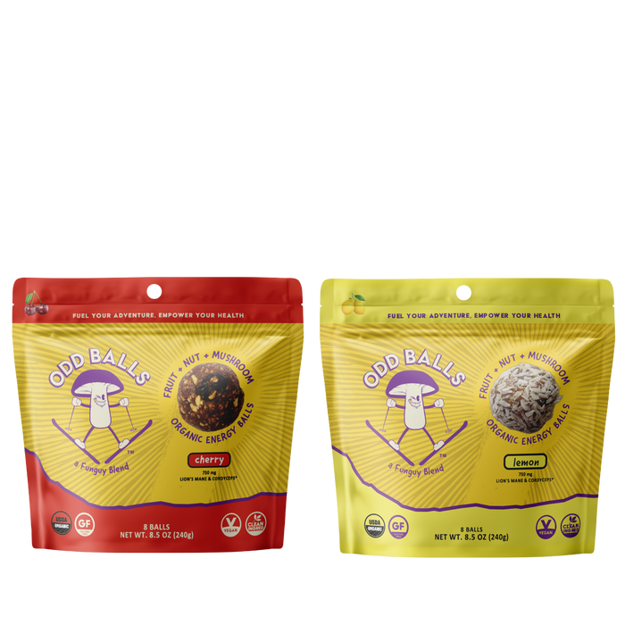 Two stand-up pouches of Odd Balls organic energy balls shown side by side on a white background. The left pouch is red and yellow, labeled cherry flavor, and the right pouch is yellow and green, labeled lemon flavor.